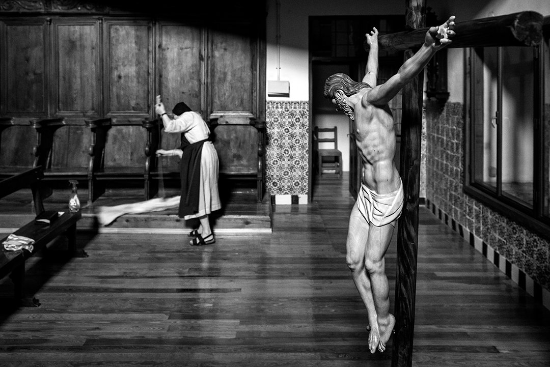 A crucifix in the foreground and a nun at the far end of a room.